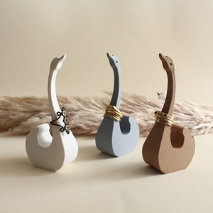 Könnte beinhalten: Drei Keramik-Schwanen-Ringhalter in Weiß, Hellblau und Braun. Jeder Schwan hat einen Ring auf seinem Hals.