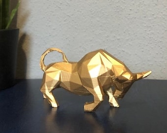 May include: A gold-colored, geometric bull sculpture with a low-poly design. The sculpture is standing on a dark blue surface.