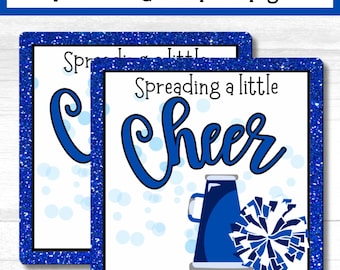 May include: Two blue and white printable cheer team tags with a blue glitter background. The tag on the right has a blue megaphone and a blue and white pom pom. The text on the tag reads "Spreading a little cheer".