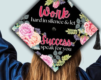 Könnte beinhalten: Ein schwarzer Abschlusskappen-Aufsatz mit einem Blumenmuster aus rosa und pfirsichfarbenen Rosen, grünen Blättern und dunklen Beeren. Der Text Work hard in silence & let Success speak for you ist in rosa Schreibschrift und weißer Serifenschrift.