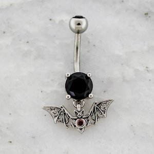 May include: A silver belly button ring with a black gem and a dangling bat charm with a red gem eye.