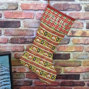 May include: A red and green Christmas stocking with a plaid cuff and the name "LaTita" embroidered on it. The stocking is hanging on a brick wall.