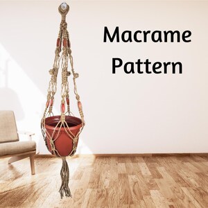 May include: A macrame plant hanger with a terracotta-colored pot. The beige-colored macrame has red beads and a tassel at the bottom. The text "Macrame Pattern" is displayed on the wall.