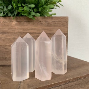 Pode incluir: Quatro pontas de cristal de quartzo rosa transparente, cada uma com um tom de rosa ligeiramente diferente, estão dispostas em uma fila sobre uma superfície de madeira.