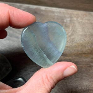 May include: A light blue heart-shaped fluorite crystal with white veins. The crystal is smooth and polished.