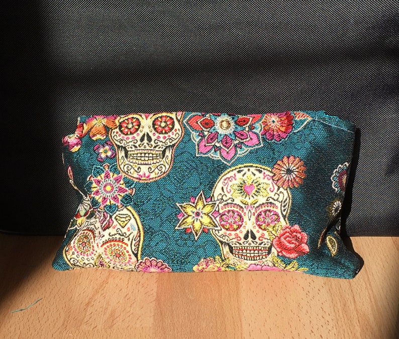 Peut inclure: Pochette en tissu bleu sarcelle avec un motif floral et cr&acirc;ne color&eacute;. Les cr&acirc;nes ont des d&eacute;tails roses, jaunes et blancs.