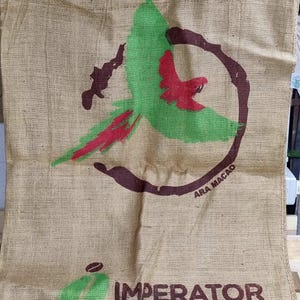 Può includere: Un sacco di juta marrone con un design di pappagallo verde e rosso e il testo "ARA MACAO" e "IMPERATOR" stampato su di esso.