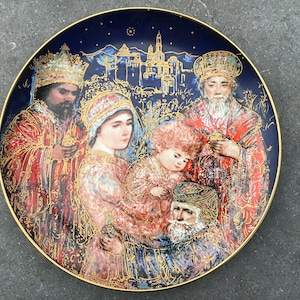 Puede incluir: Un plato de cerámica azul y dorado con una representación de los tres reyes magos visitando al niño Jesús. El plato presenta una ilustración detallada con detalles dorados y un fondo azul oscuro.