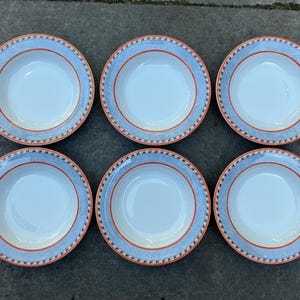 May include: Six white ceramic bowls with a blue and orange decorative border. The bowls are arranged in two rows of three, showcasing a classic design. The rims feature a blue band with an orange inner ring and a patterned edge.