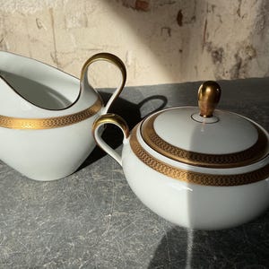 Può includere: Una tazza di ceramica bianca con manico nero e la scritta "But First, Coffee" in grassetto nero. La tazza è posta su uno sfondo sfocato, suggerendo un'ambientazione accogliente.