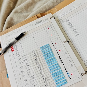 May include: A white planner with a brown leather cover. The planner has a tab that says "TOTALLY got this!" and a calendar with dates and times. The calendar is filled with blue and pink stickers. The planner is open to a page with the text "The best is yet to come."