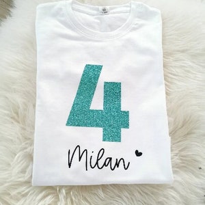 Könnte beinhalten: Weißes T-Shirt mit einer türkisfarbenen Glitzerzahl 4 und dem Namen "Milan" darunter.