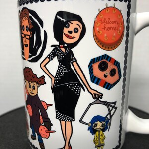 May include: White ceramic mug featuring illustrations of characters from a movie. The mug has a black button border and a handle. The characters include a woman in a black dress, a boy in a purple coat, and a girl in a yellow raincoat. The mug also has the text "welcome home!"