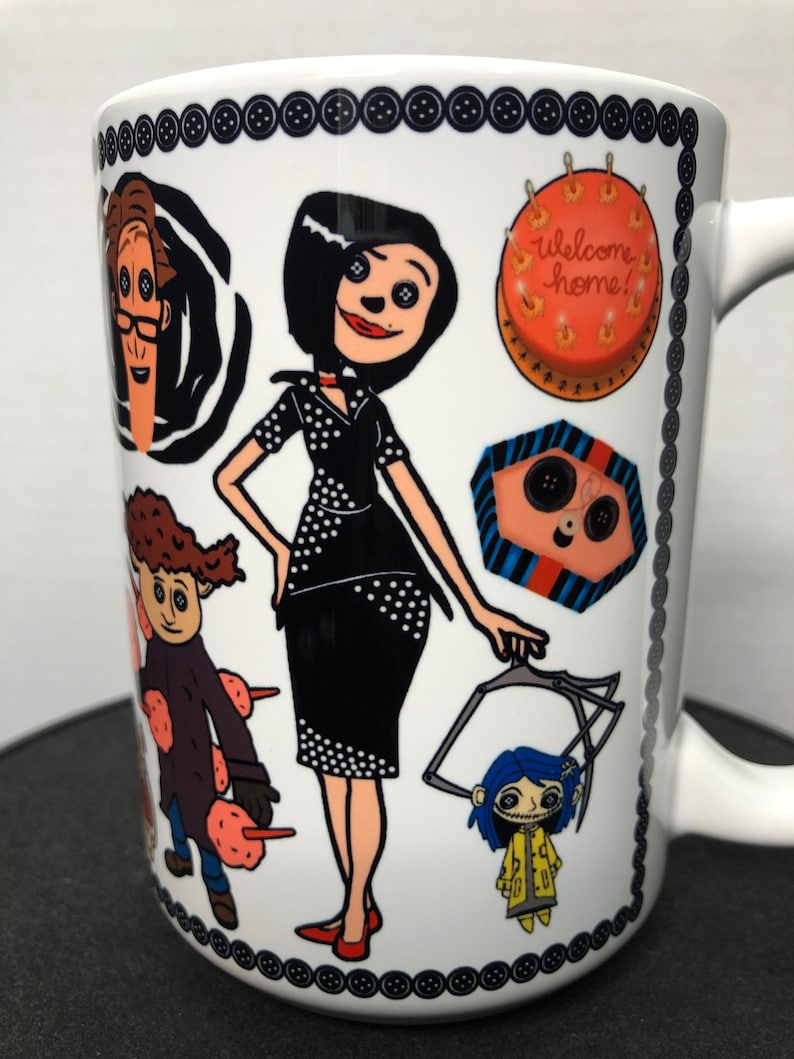 May include: White ceramic mug featuring illustrations of characters from a movie. The mug has a black button border and a handle. The characters include a woman in a black dress, a boy in a purple coat, and a girl in a yellow raincoat. The mug also has the text "welcome home!"