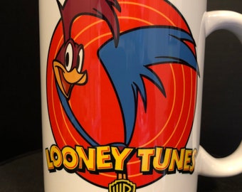 May include: White ceramic mug with a red, white, and blue Road Runner cartoon character from Looney Tunes. The mug has the Warner Bros. logo and the words "Looney Tunes" printed on it.