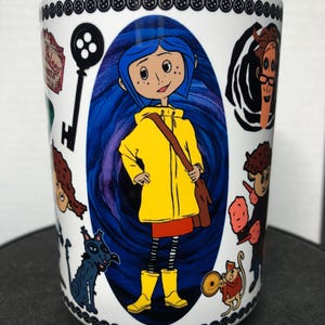 May include: White ceramic mug featuring illustrations from the animated film. The central image is of a girl in a yellow raincoat and boots, surrounded by other characters and imagery from the movie. The top and bottom of the mug are decorated with black button designs.