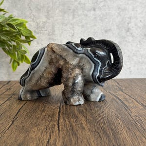 May include: A black and white agate elephant sculpture. The elephant is carved in a standing position with its trunk raised. The agate has a natural, banded pattern.