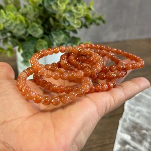 May include: A stack of orange sunstone bead bracelets. The bracelets are made with small, round beads and have a natural, earthy look.