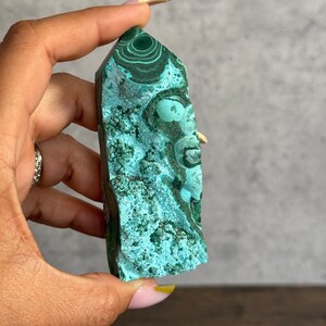 Puede incluir: Una punta de cristal de malaquita verde con un patr&oacute;n de remolino. El cristal es liso y pulido.