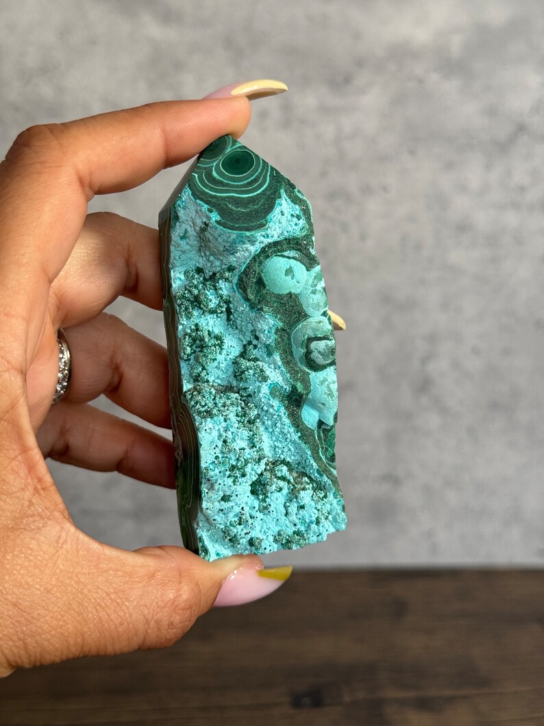 Puede incluir: Una punta de cristal de malaquita verde con un patr&oacute;n de remolino. El cristal es liso y pulido.