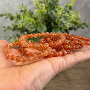May include: A stack of orange sunstone beaded bracelets. The bracelets are made of small, round beads and are strung on elastic.