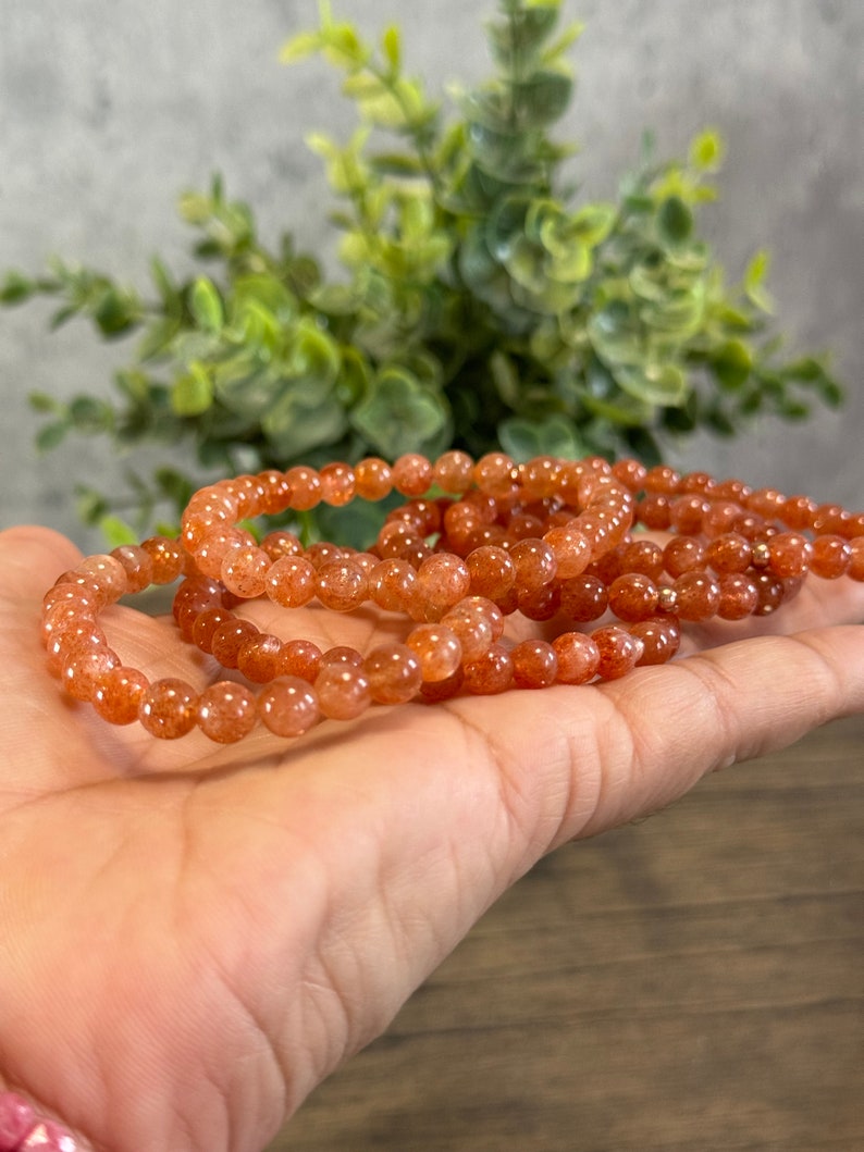 May include: A stack of orange sunstone beaded bracelets. The bracelets are made of small, round beads and are strung on elastic.