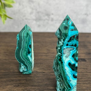 Puede incluir: Dos torres de cristal de azurita malaquita verde y azul sobre una superficie de madera. Las torres son puntiagudas en la parte superior y tienen una textura natural y rugosa.