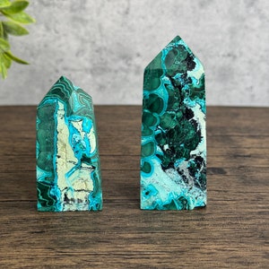 Puede incluir: Dos puntas de cristal de azurita malaquita verde y azul sobre una superficie de madera. La punta m&aacute;s grande est&aacute; a la derecha y la m&aacute;s peque&ntilde;a a la izquierda.