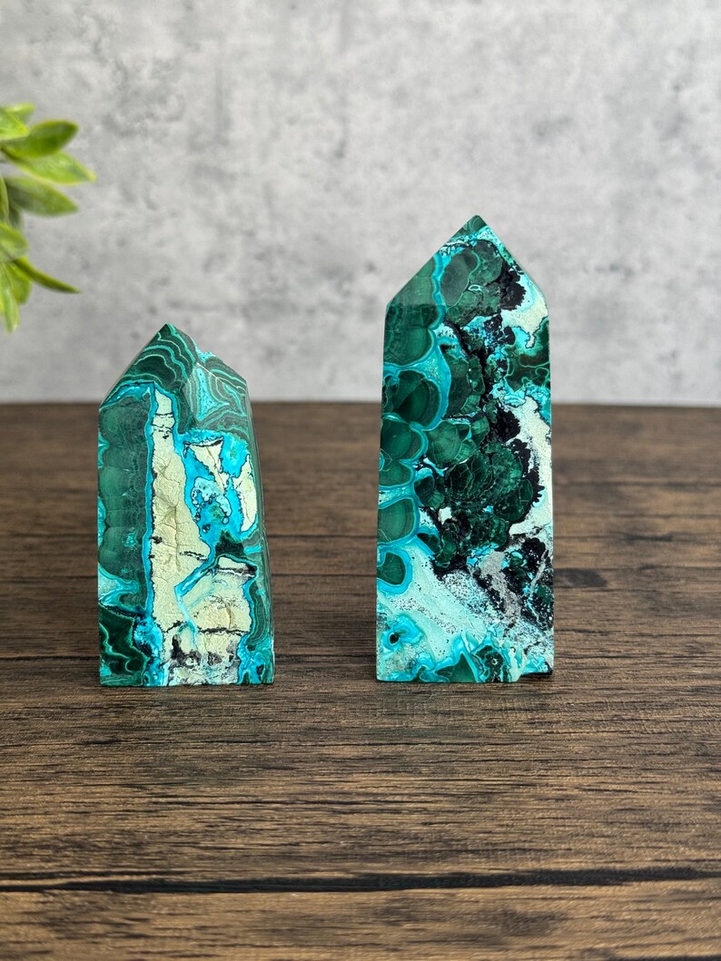 Puede incluir: Dos puntas de cristal de azurita malaquita verde y azul sobre una superficie de madera. La punta m&aacute;s grande est&aacute; a la derecha y la m&aacute;s peque&ntilde;a a la izquierda.