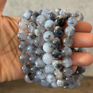 May include: A stack of gray and white dendritic agate bead bracelets. The beads are round and have a natural, organic look.