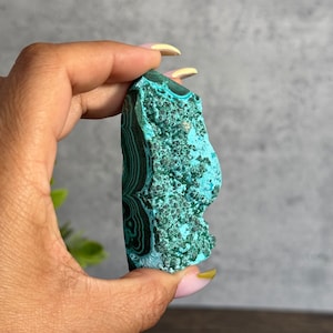 Puede incluir: Un cristal de malaquita en bruto, verde y azul, con un patr&oacute;n de remolino. El cristal mide aproximadamente 5 cm de largo y 2 cm de ancho.