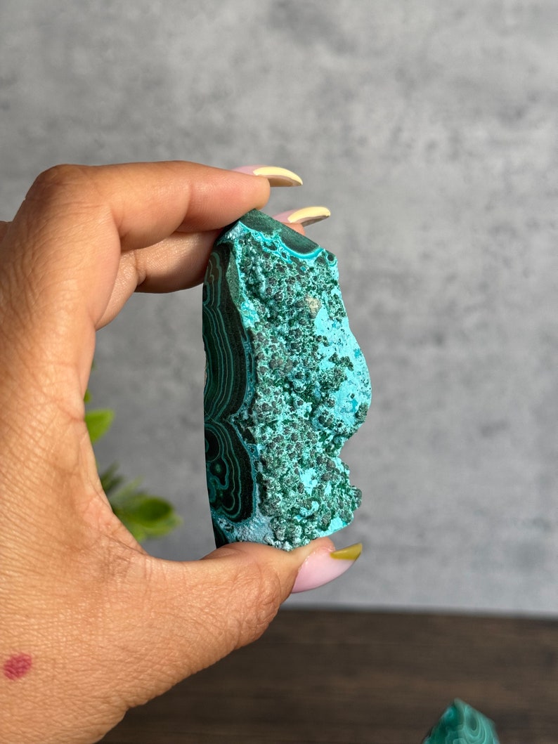 Puede incluir: Un cristal de malaquita en bruto, verde y azul, con un patr&oacute;n de remolino. El cristal mide aproximadamente 5 cm de largo y 2 cm de ancho.