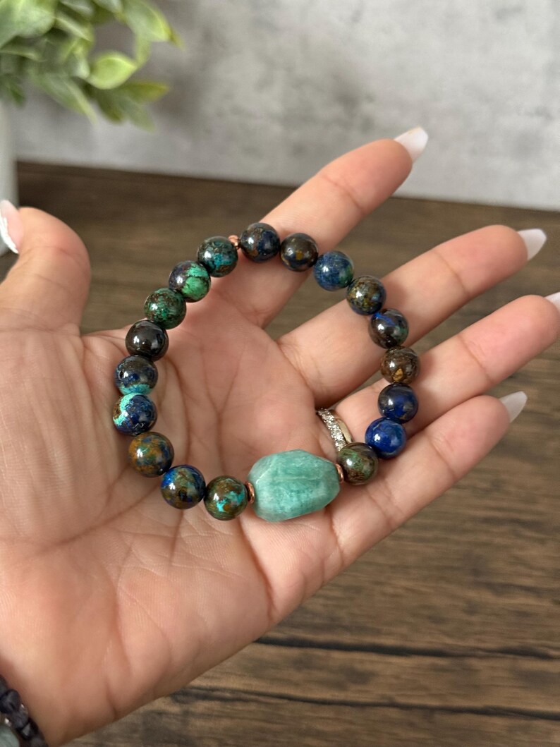 May include: A beaded bracelet with green, blue, and brown stones. The bracelet has a larger, light green stone in the center.