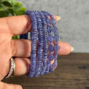 Puede incluir: Un conjunto de cinco pulseras de piedras azules con diferentes tama&ntilde;os y formas de cuentas. Las pulseras est&aacute;n apiladas una encima de la otra y se sostienen en una mano.
