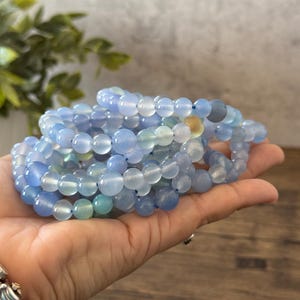 Puede incluir: Una pila de pulseras de cuentas de &aacute;gata azul. Las cuentas son redondas y lisas, y las pulseras est&aacute;n hechas con el&aacute;stico.