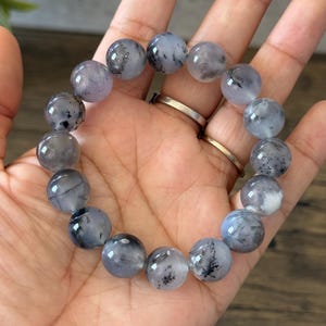 May include: A bracelet made of round, gray and white beads with black flecks. The beads are strung on a clear elastic cord.