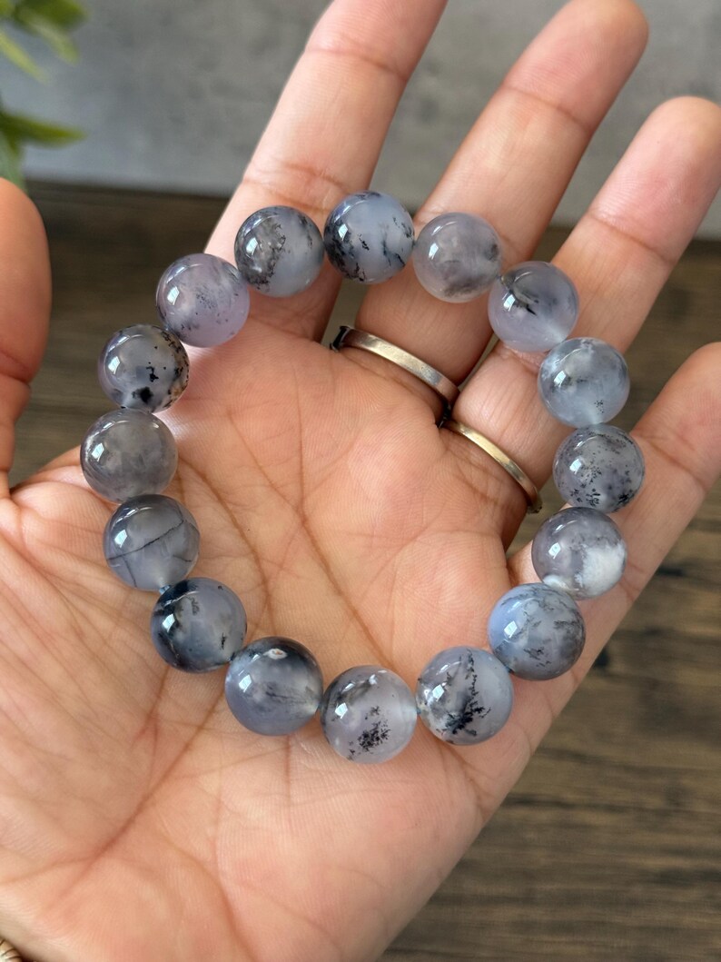 May include: A bracelet made of round, gray and white beads with black flecks. The beads are strung on a clear elastic cord.
