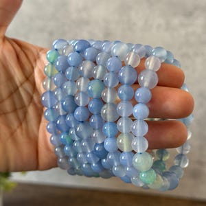 Puede incluir: Una pila de cuentas redondas y lisas de &aacute;gata azul claro. Las cuentas est&aacute;n enhebradas para formar un brazalete.