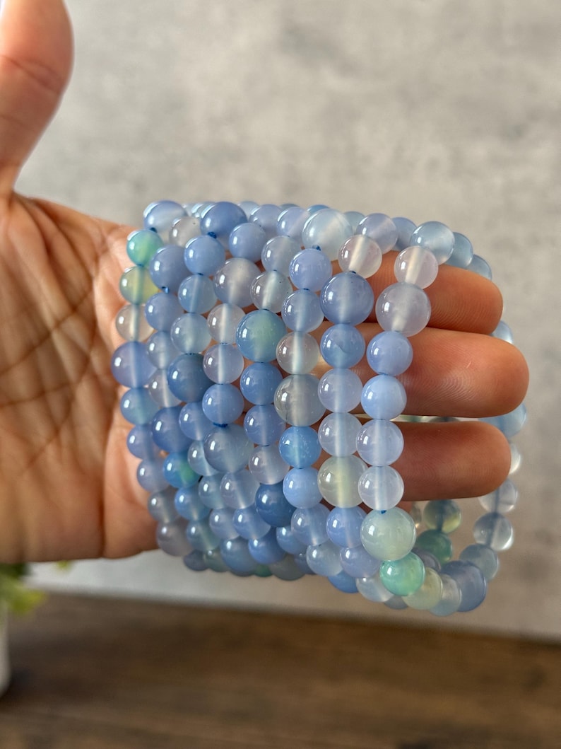 Puede incluir: Una pila de cuentas redondas y lisas de &aacute;gata azul claro. Las cuentas est&aacute;n enhebradas para formar un brazalete.