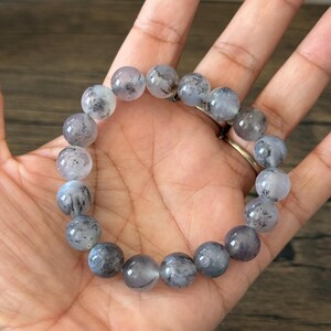 May include: A bracelet made of round, gray and white beads with black flecks. The beads are strung on an elastic cord.