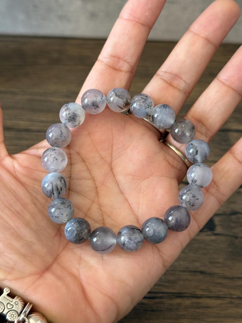 May include: A bracelet made of round, gray and white beads with black flecks. The beads are strung on an elastic cord.