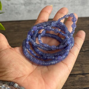 Puede incluir: Un conjunto de pulseras de piedras preciosas azules hechas de peque&ntilde;as cuentas redondas. Las pulseras est&aacute;n apiladas una encima de la otra y se sostienen en una mano.