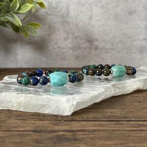 May include: Two beaded bracelets with a turquoise green stone accent. The bracelets are made with dark brown, blue, and green beads.