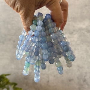Puede incluir: Una pila de pulseras de cuentas de &aacute;gata azul. Las cuentas son redondas y tienen un acabado liso y pulido. Las pulseras son de diferentes longitudes y tienen una sutil variaci&oacute;n de color.