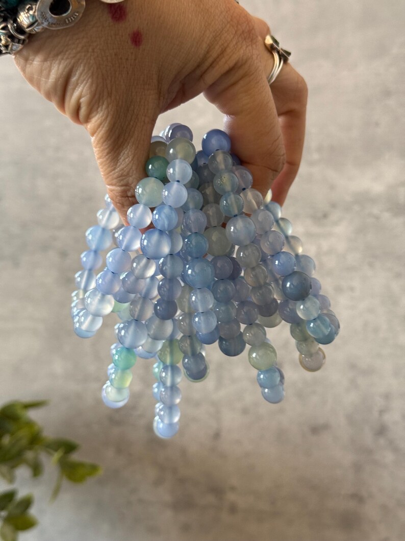 Puede incluir: Una pila de pulseras de cuentas de &aacute;gata azul. Las cuentas son redondas y tienen un acabado liso y pulido. Las pulseras son de diferentes longitudes y tienen una sutil variaci&oacute;n de color.