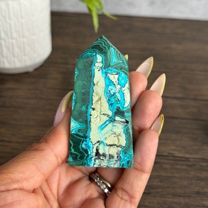 Puede incluir: Una punta de cristal de malaquita verde y azul con un patr&oacute;n &uacute;nico de remolinos y vetas. El cristal es liso y pulido, y tiene una forma natural y org&aacute;nica.