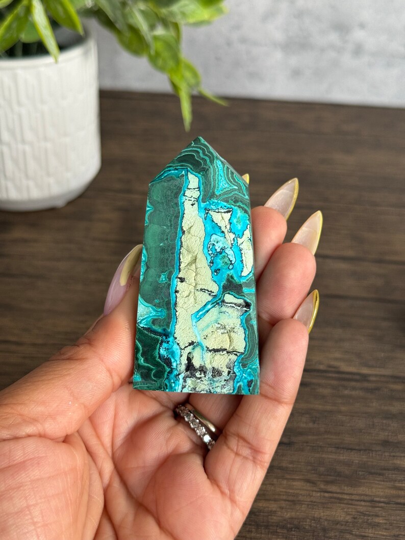 Puede incluir: Una punta de cristal de malaquita verde y azul con un patr&oacute;n &uacute;nico de remolinos y vetas. El cristal es liso y pulido, y tiene una forma natural y org&aacute;nica.