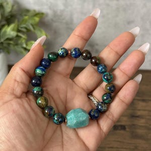 May include: A green, blue, and brown beaded bracelet with a large, light green gemstone charm.