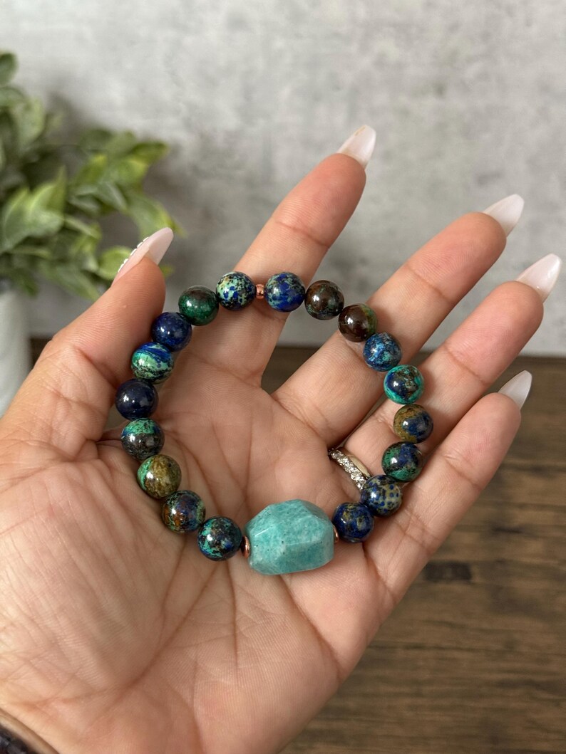 May include: A green, blue, and brown beaded bracelet with a large, light green gemstone charm.