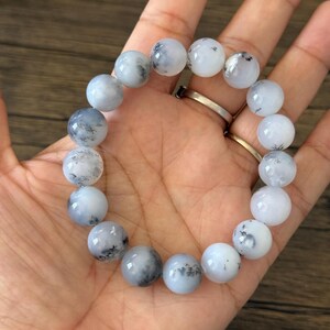 May include: A white and gray beaded bracelet with black flecks throughout the beads. The bracelet is made of round beads and is approximately 7 inches in length.